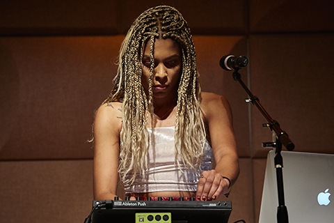 A woman with blonde braided hair adjusts a setting on a drum machine 