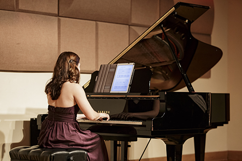 A woman in a maroon dress with long hair is playing a black Yamaha grand piano