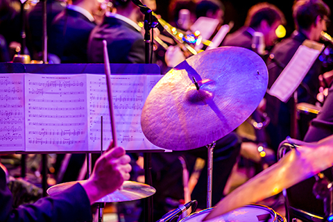 A drum stick heading towards a cymbal with sheet music being displayed in the background