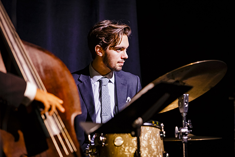 A drummer takes a moments rest and looks ahead as a bass is being played in the foreground